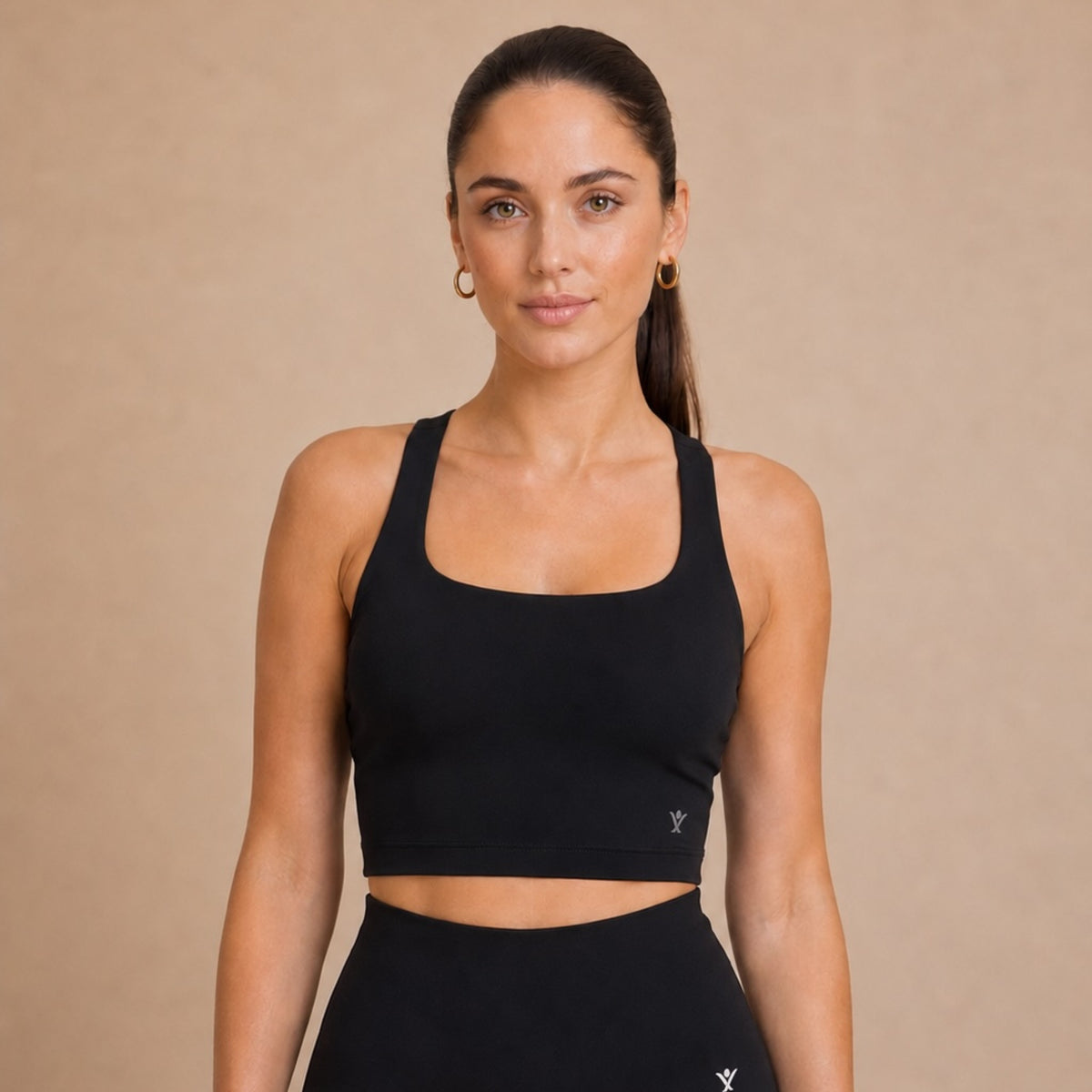 A woman modeling a black athletic crop top and matching high-waisted leggings against a solid beige studio background.
